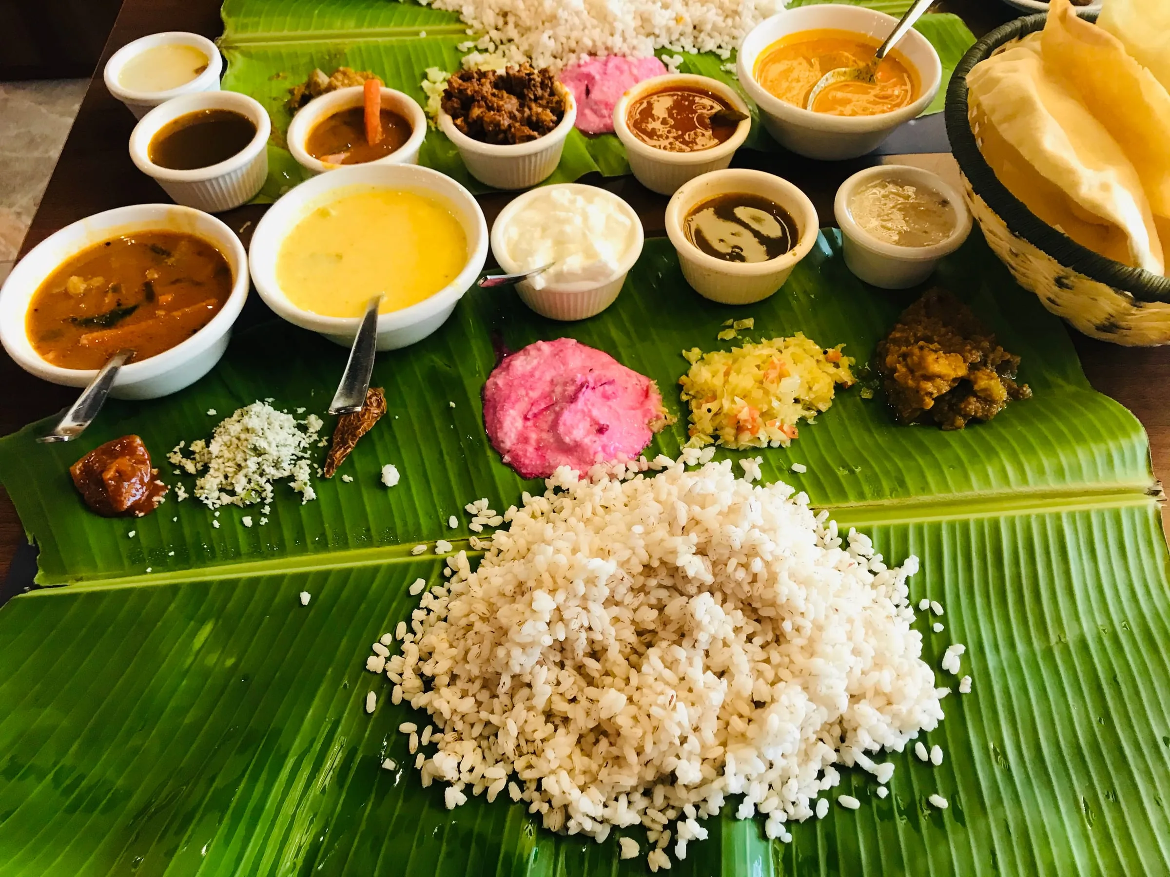 A meal served on a banana leaf, rice surrounded by small bowls of curries and sides