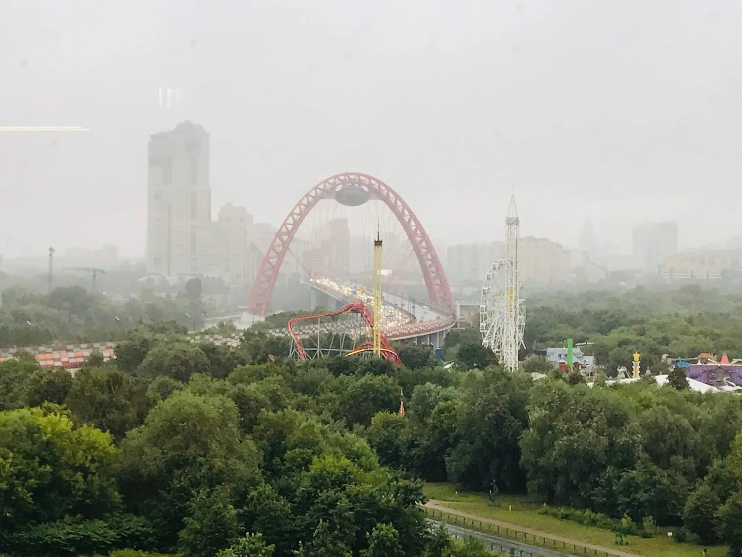 A red arched bridge and city towers half hidden in mist over a stretch of green trees