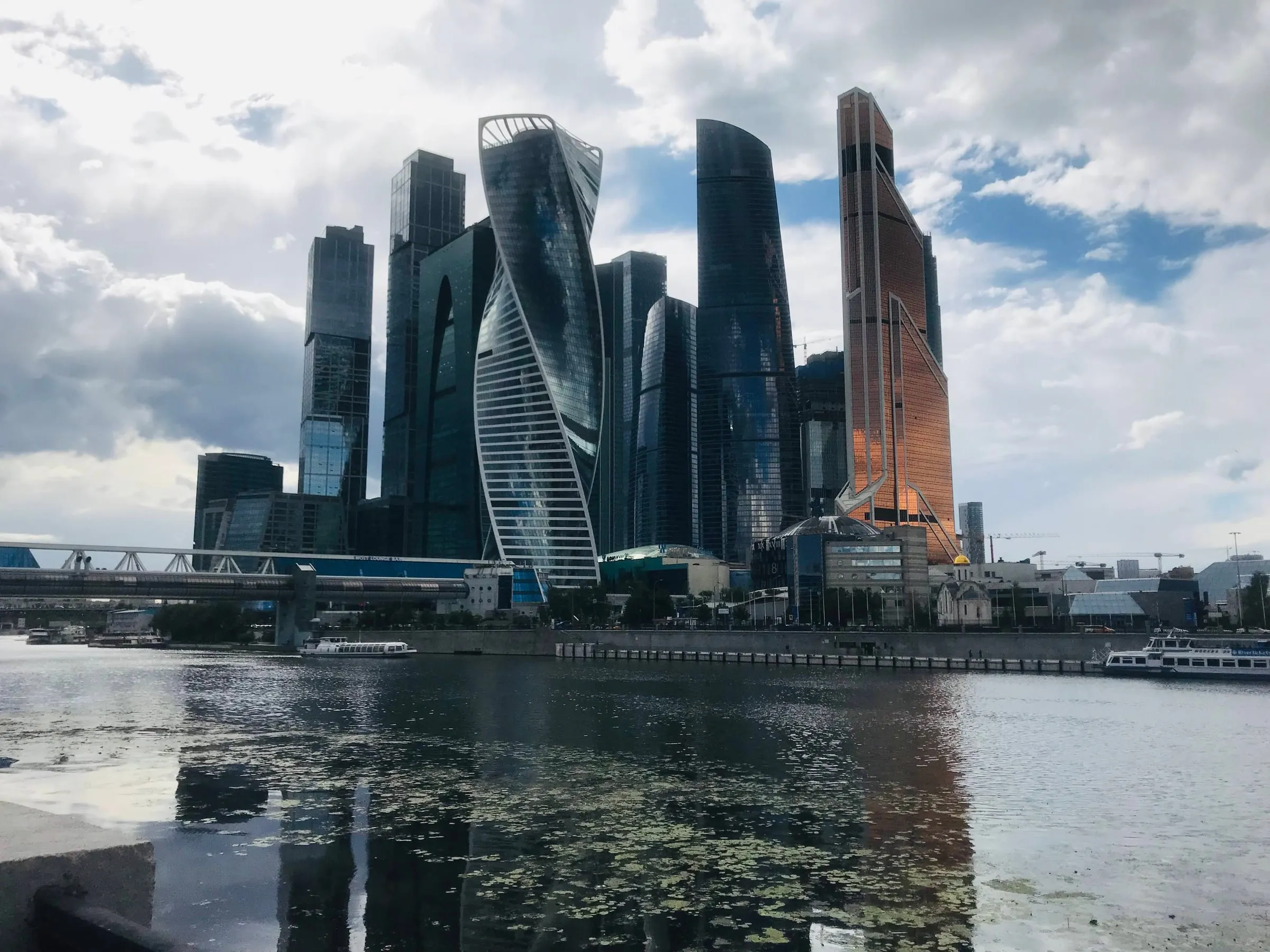 A cluster of glass skyscrapers, one twisting as it rises, across the river