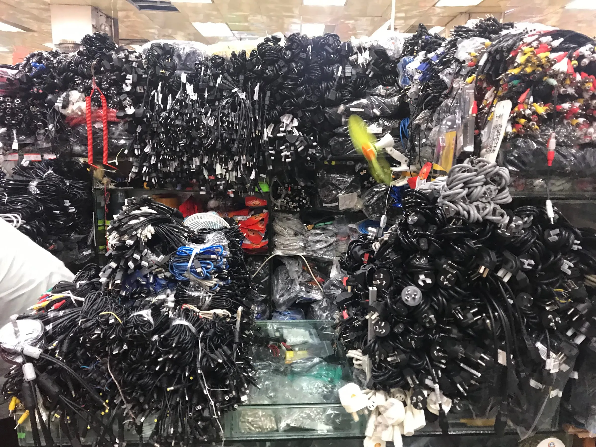 Bundles of black cables and chargers piled high on a crowded electronics market stall