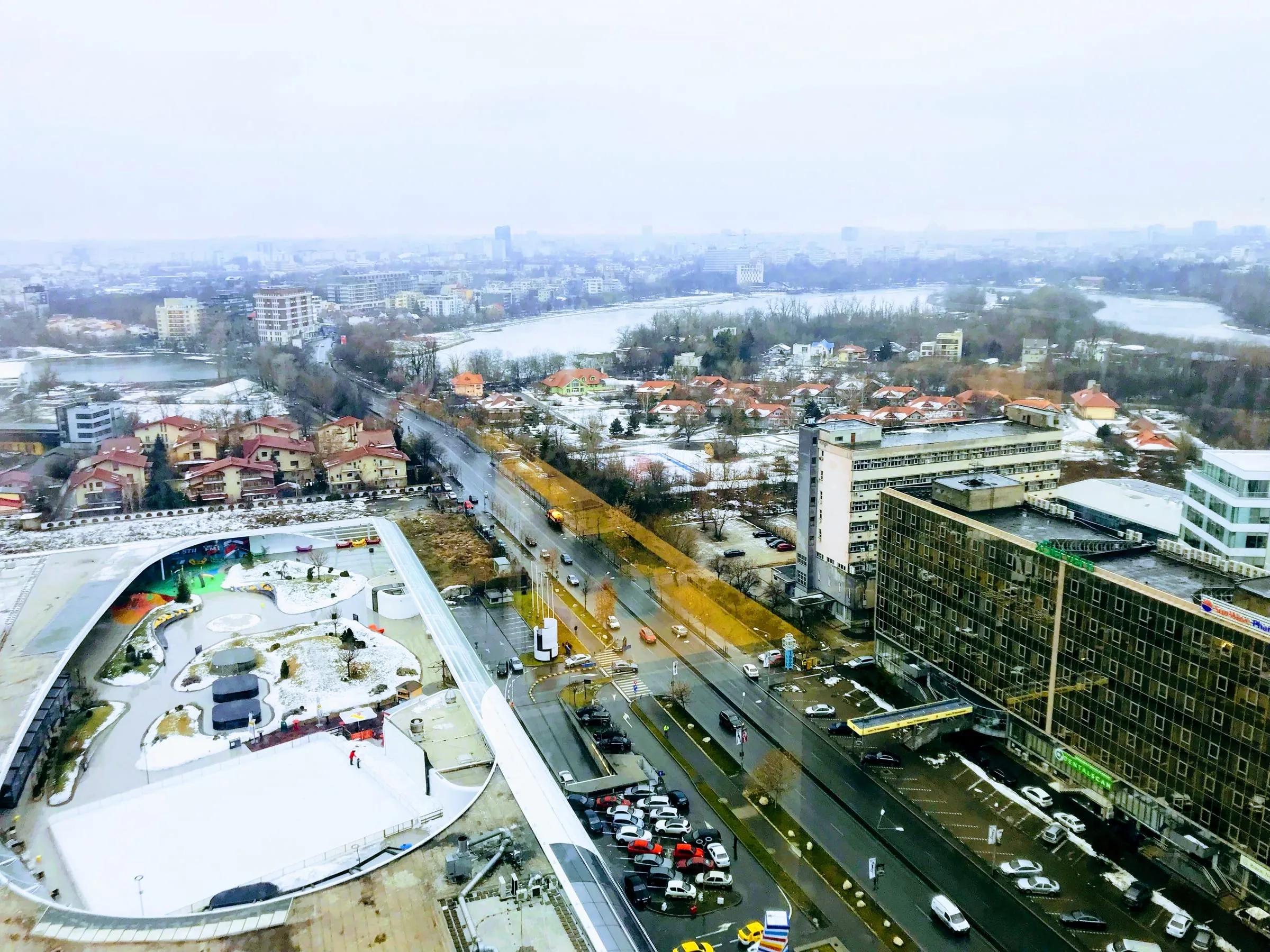 The city seen from a high window on a wet winter day, a busy road, rooftops and a lake in the distance