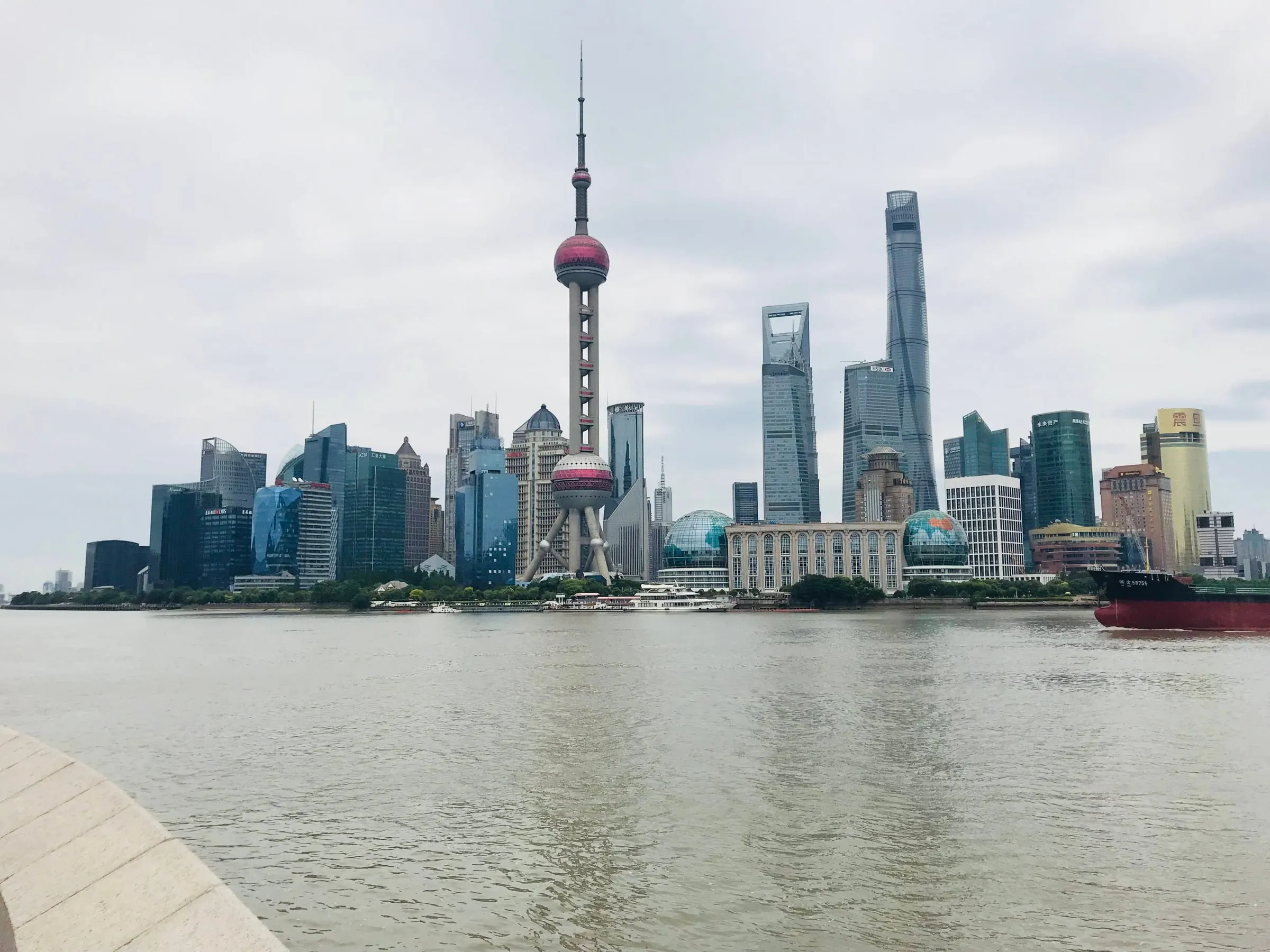 The Pudong skyline across the Huangpu river on a grey day, the Oriental Pearl Tower and Shanghai Tower rising above it