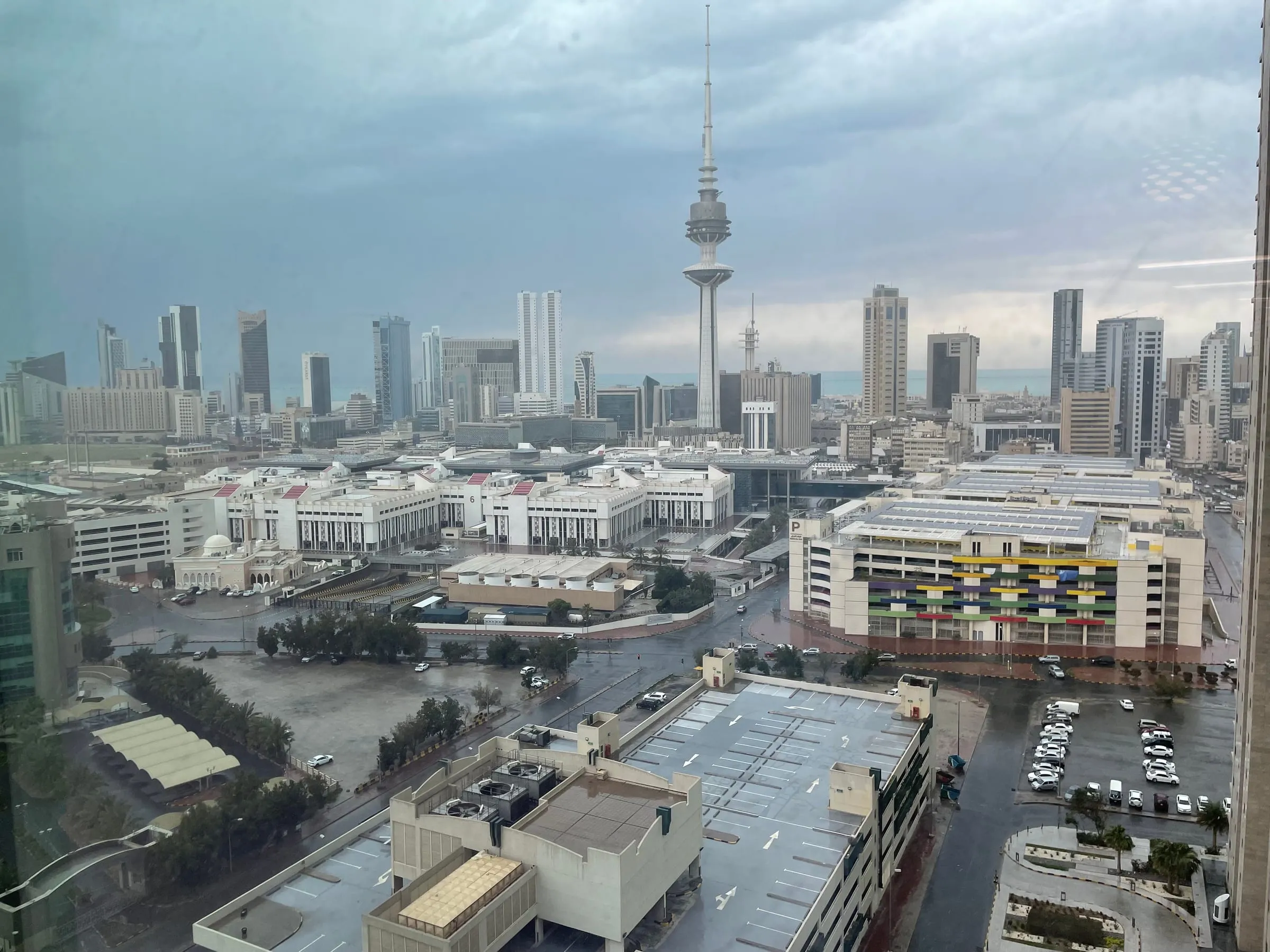 The Kuwait City skyline under heavy grey clouds, the Liberation Tower rising above office blocks
