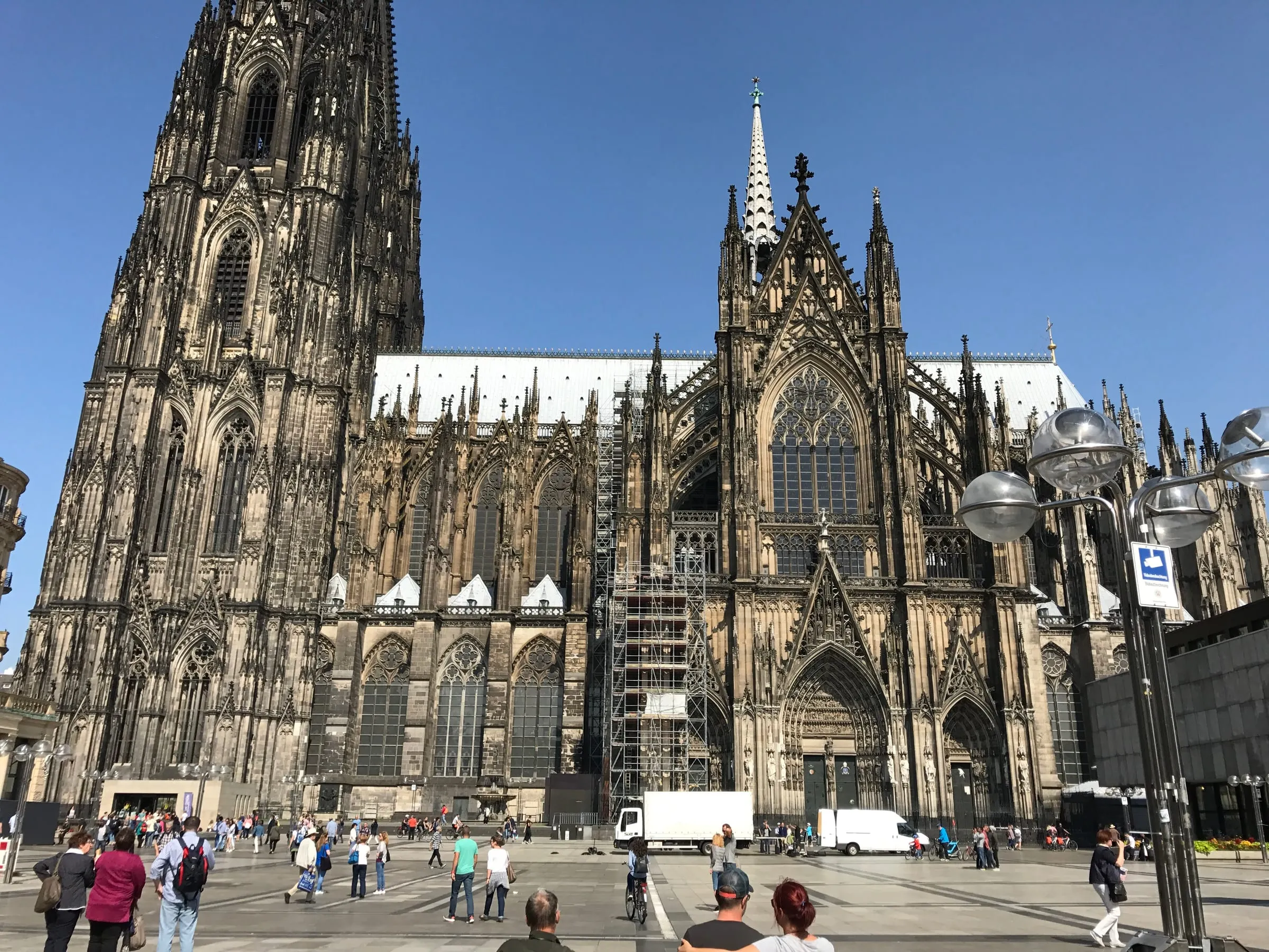 The Gothic front and spires of Cologne Cathedral under a clear blue sky, people crossing the square in front