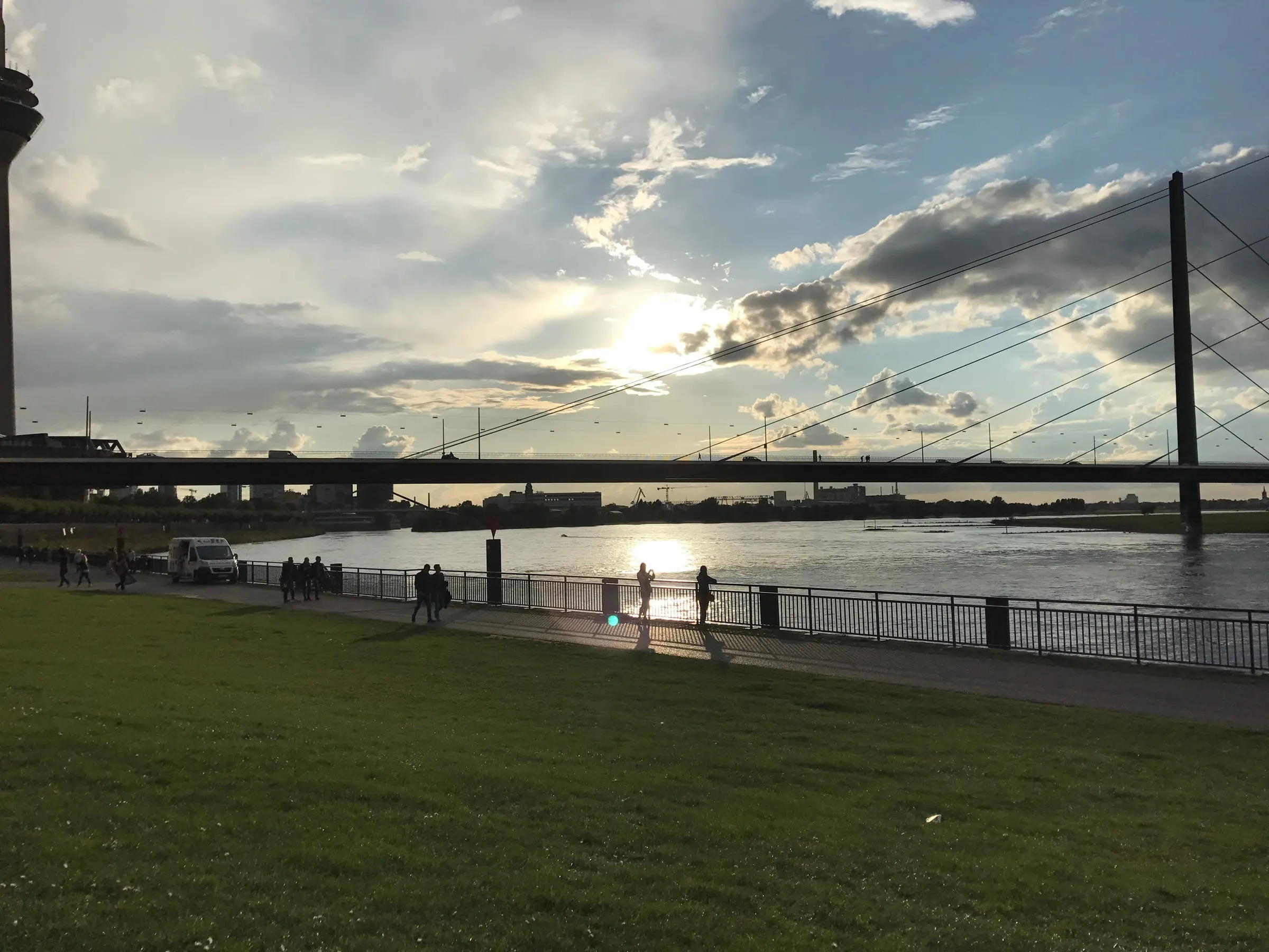 Sunset over the Rhine, a cable-stayed bridge in silhouette and people walking along the riverside