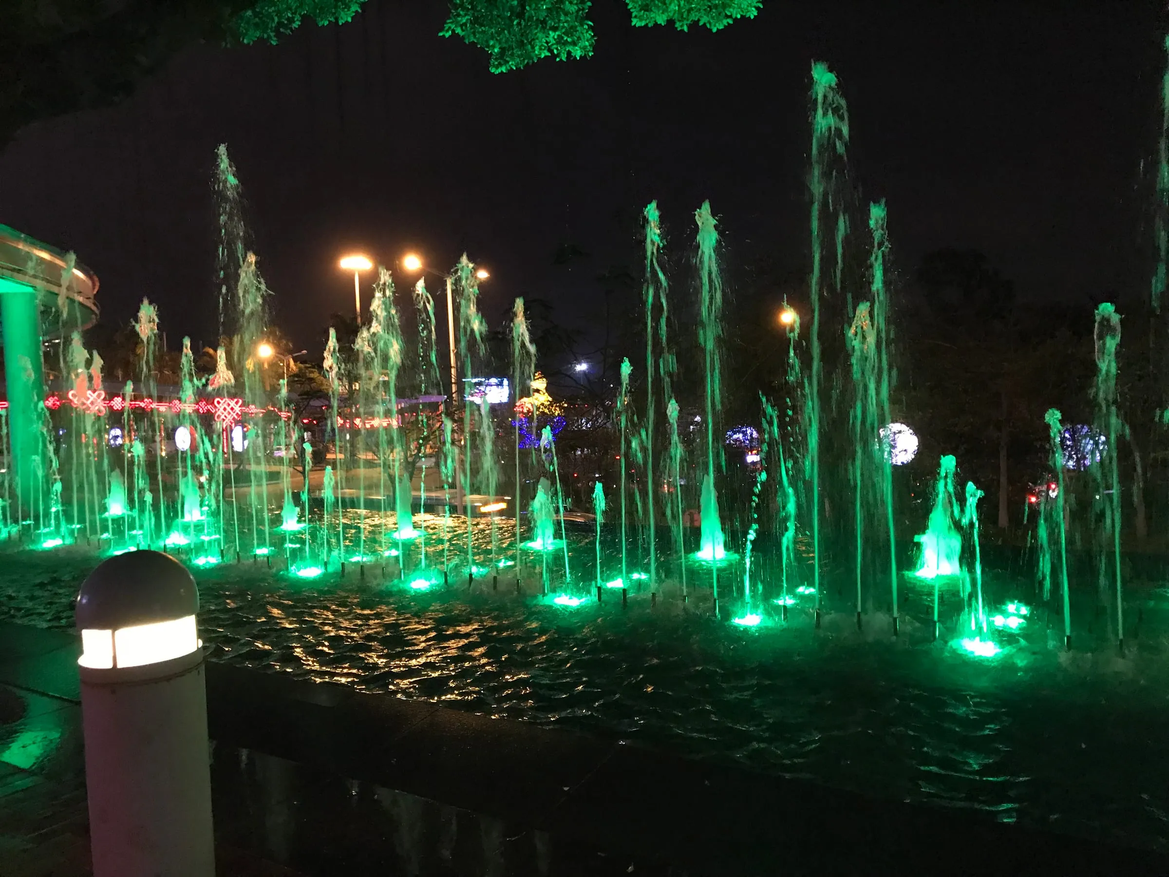 Fountains lit bright green at night, jets of water rising from a dark pool