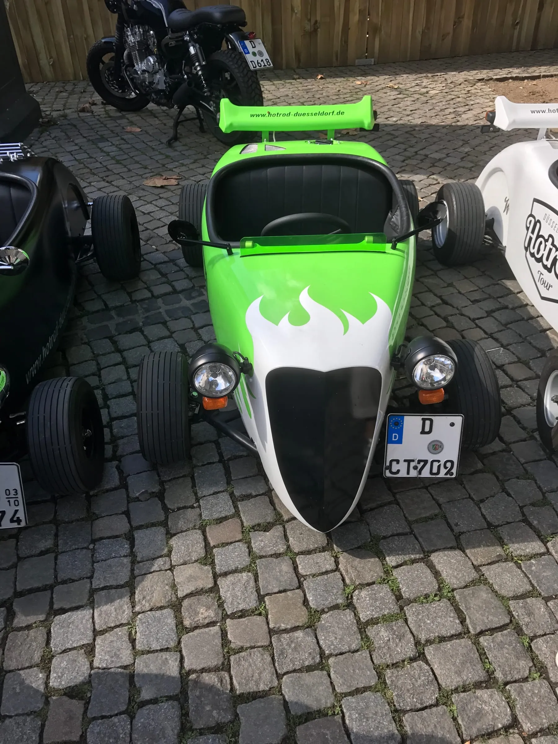 A small green and white hot rod with flame paintwork parked on cobblestones