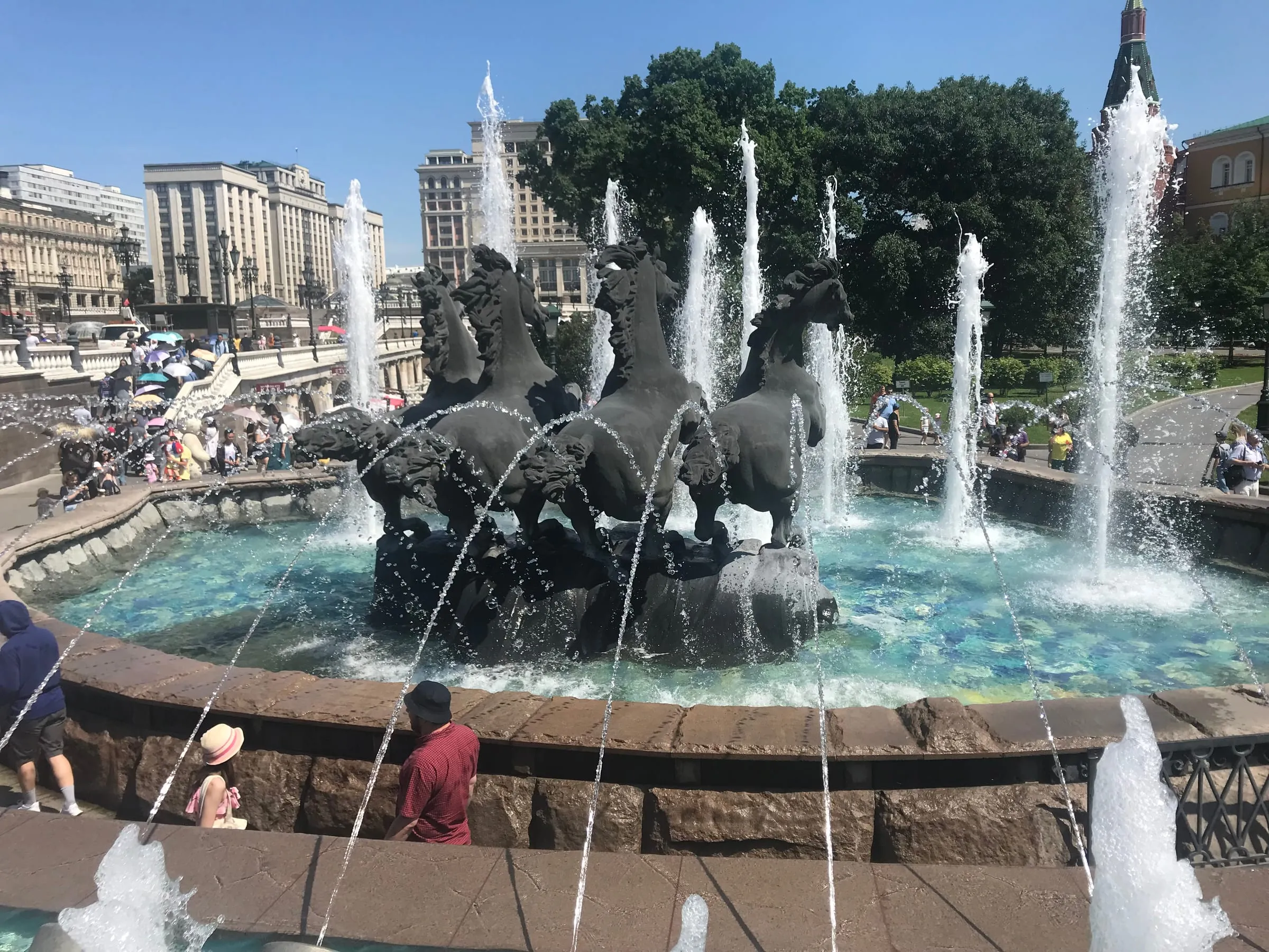A fountain with bronze horses rearing out of the water, sprays rising around them in the sun