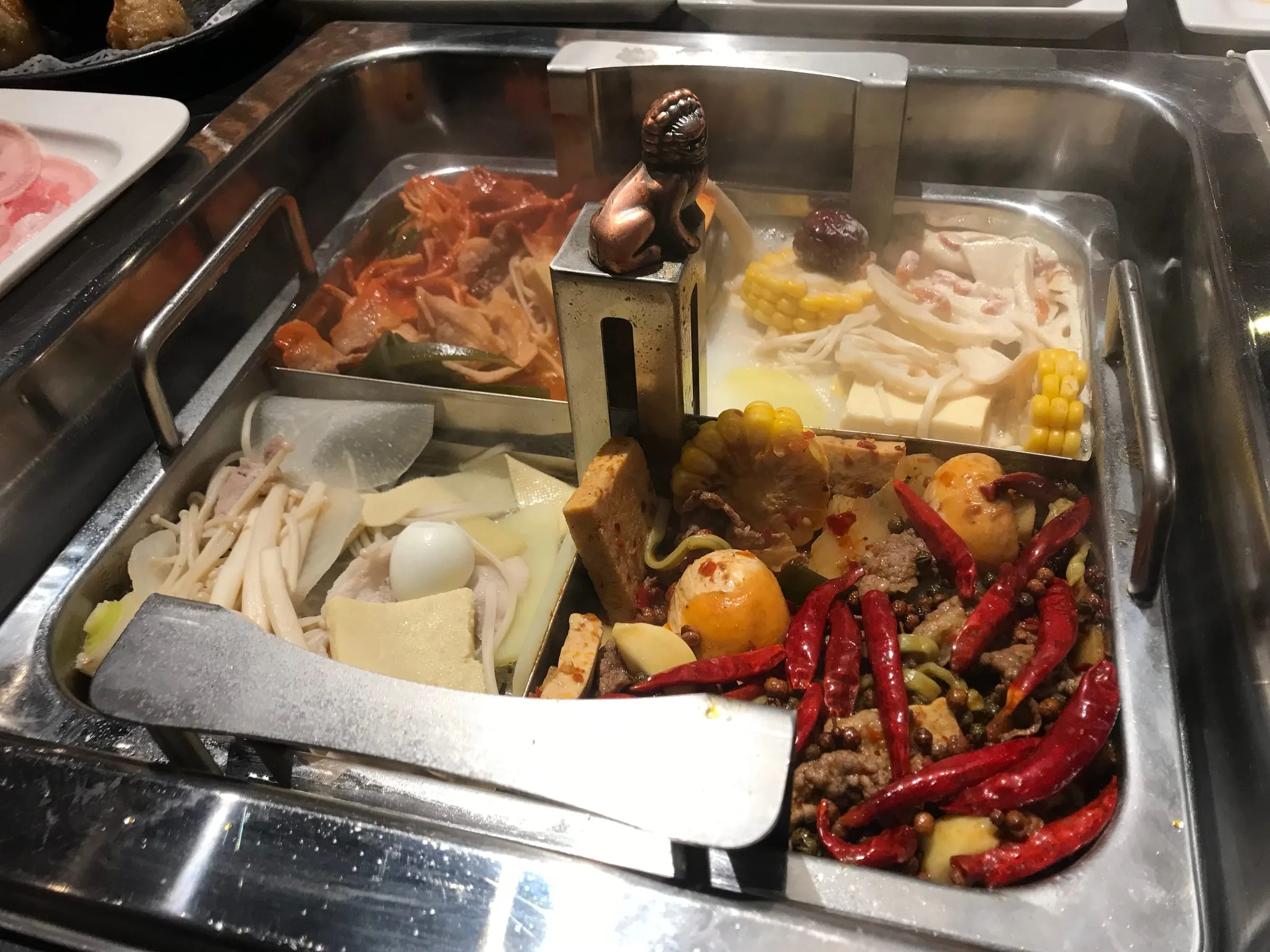A steaming hotpot with two broths, chillies and vegetables, on a crowded dinner table