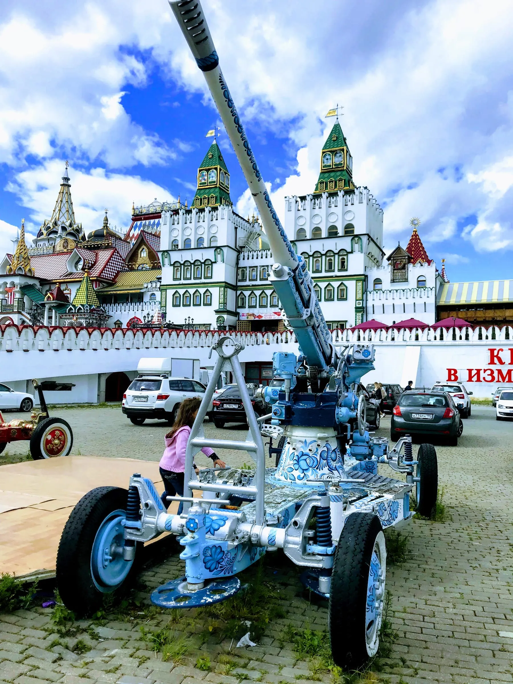 A painted anti-aircraft gun on display in front of colourful wooden buildings with pointed roofs