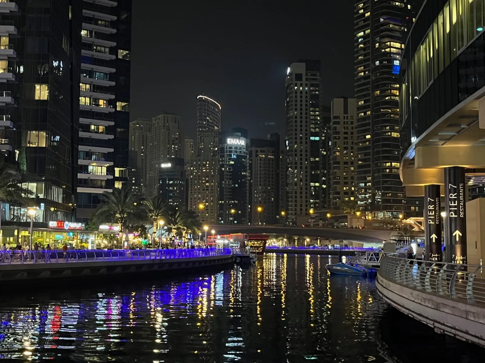 Dubai Marina at night, towers lit up on both sides and their lights reflected in the water, a Pier 7 sign on the right