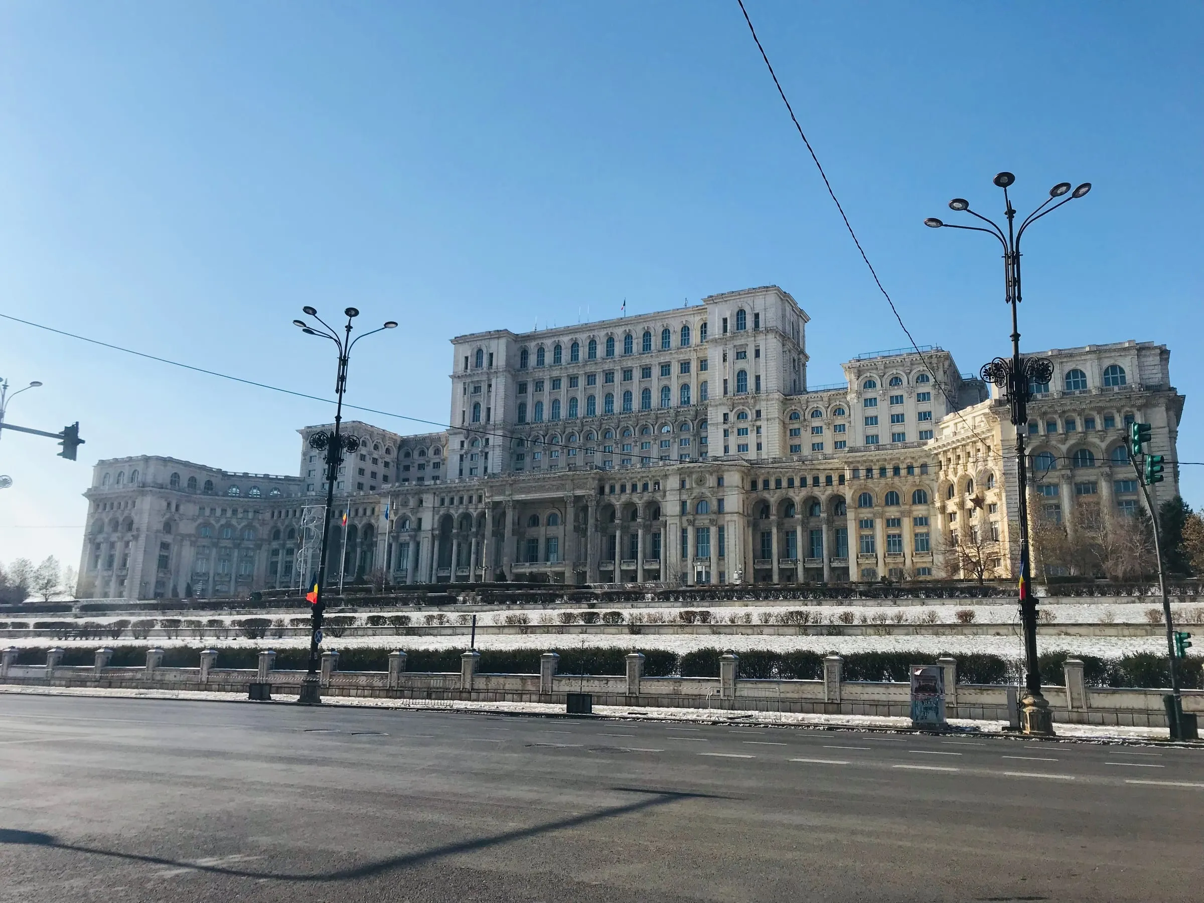 The Palace of the Parliament under a clear blue winter sky, with ornate street lamps in front