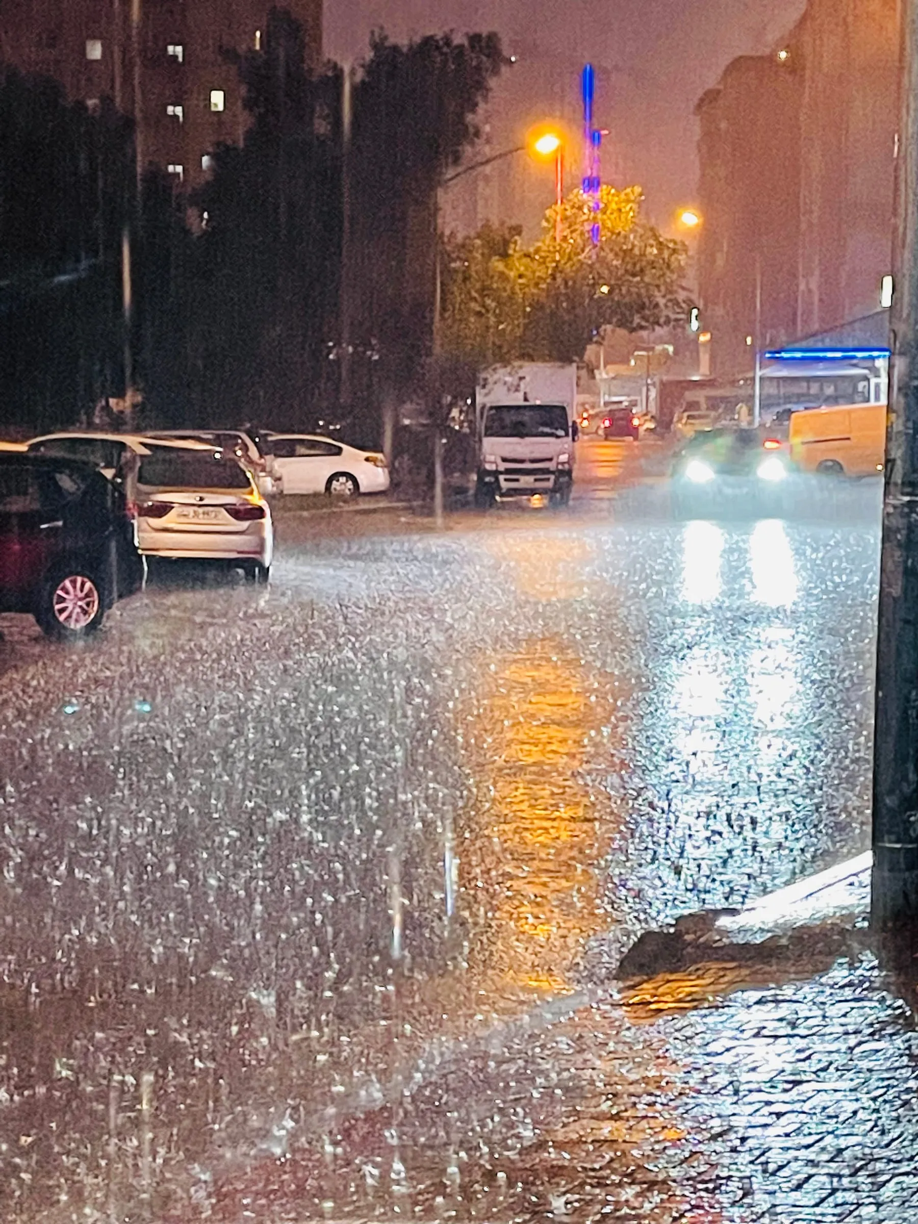 Heavy rain on a street at night, water pooling on the road under orange streetlights