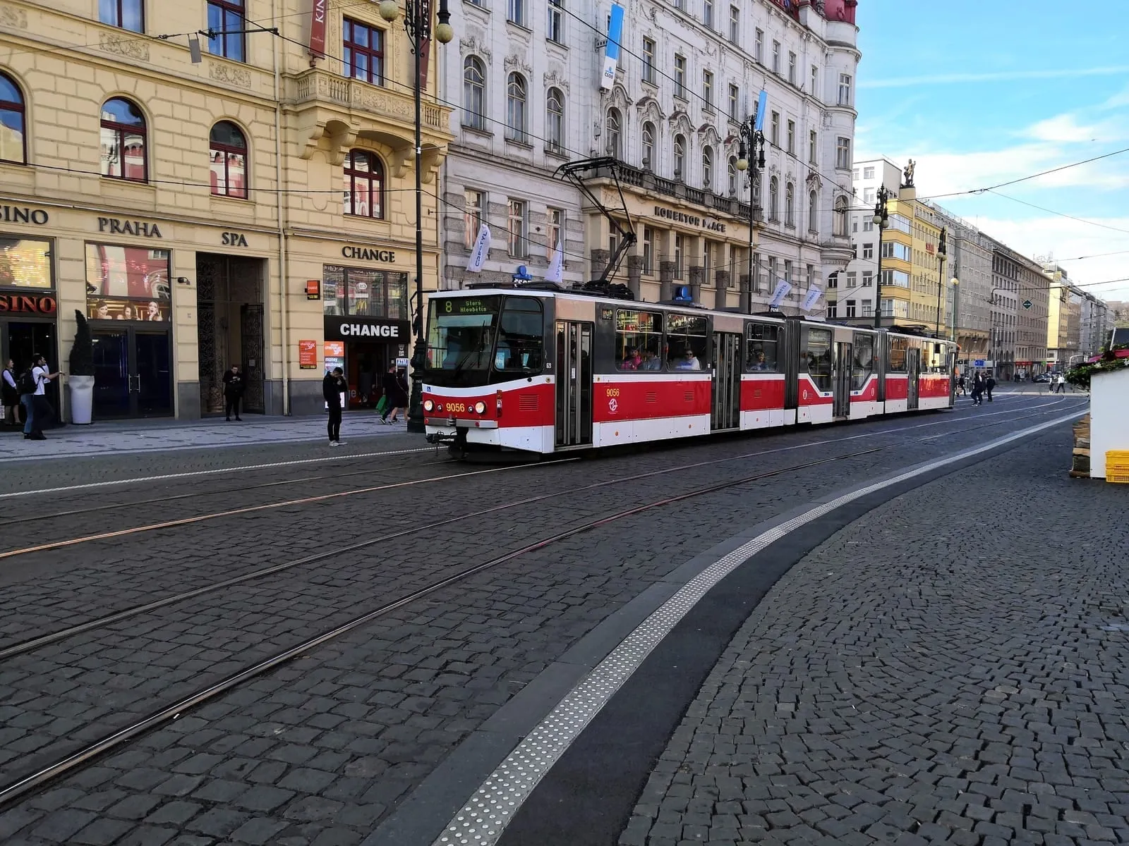 A red and white tram on a cobbled street between old buildings
