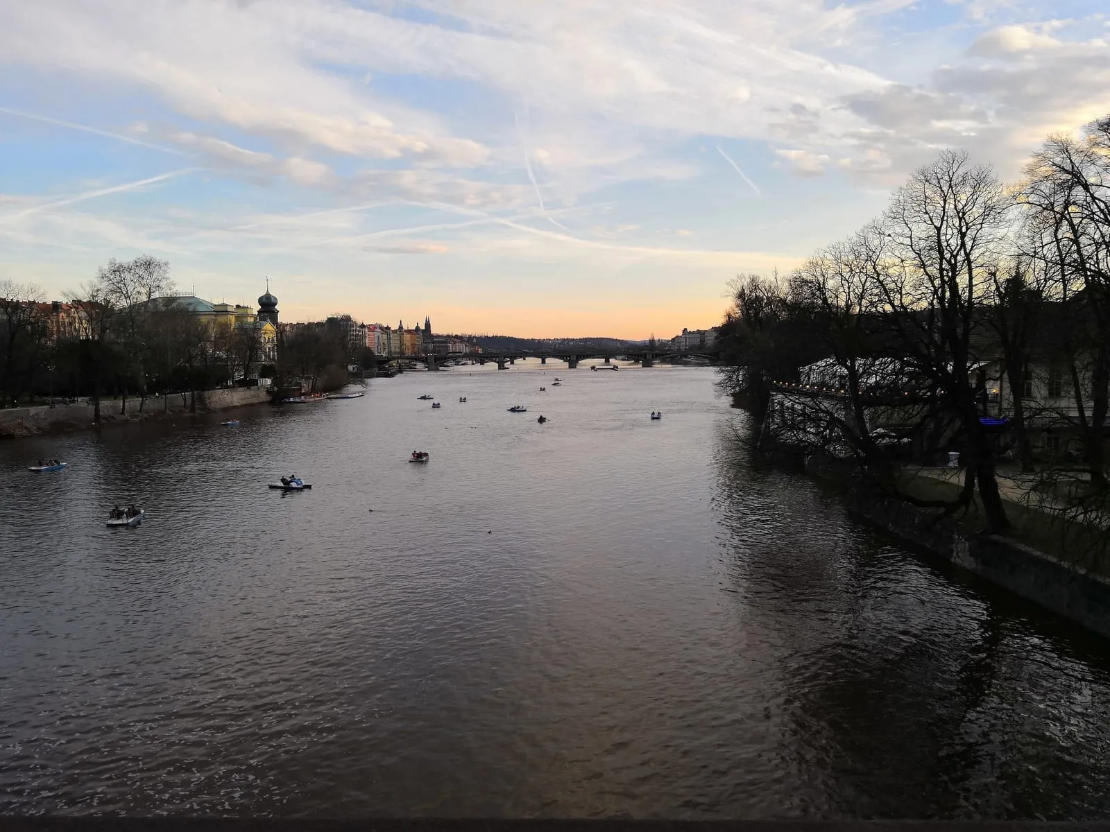 The river at dusk with small boats on the water and bare trees along the bank