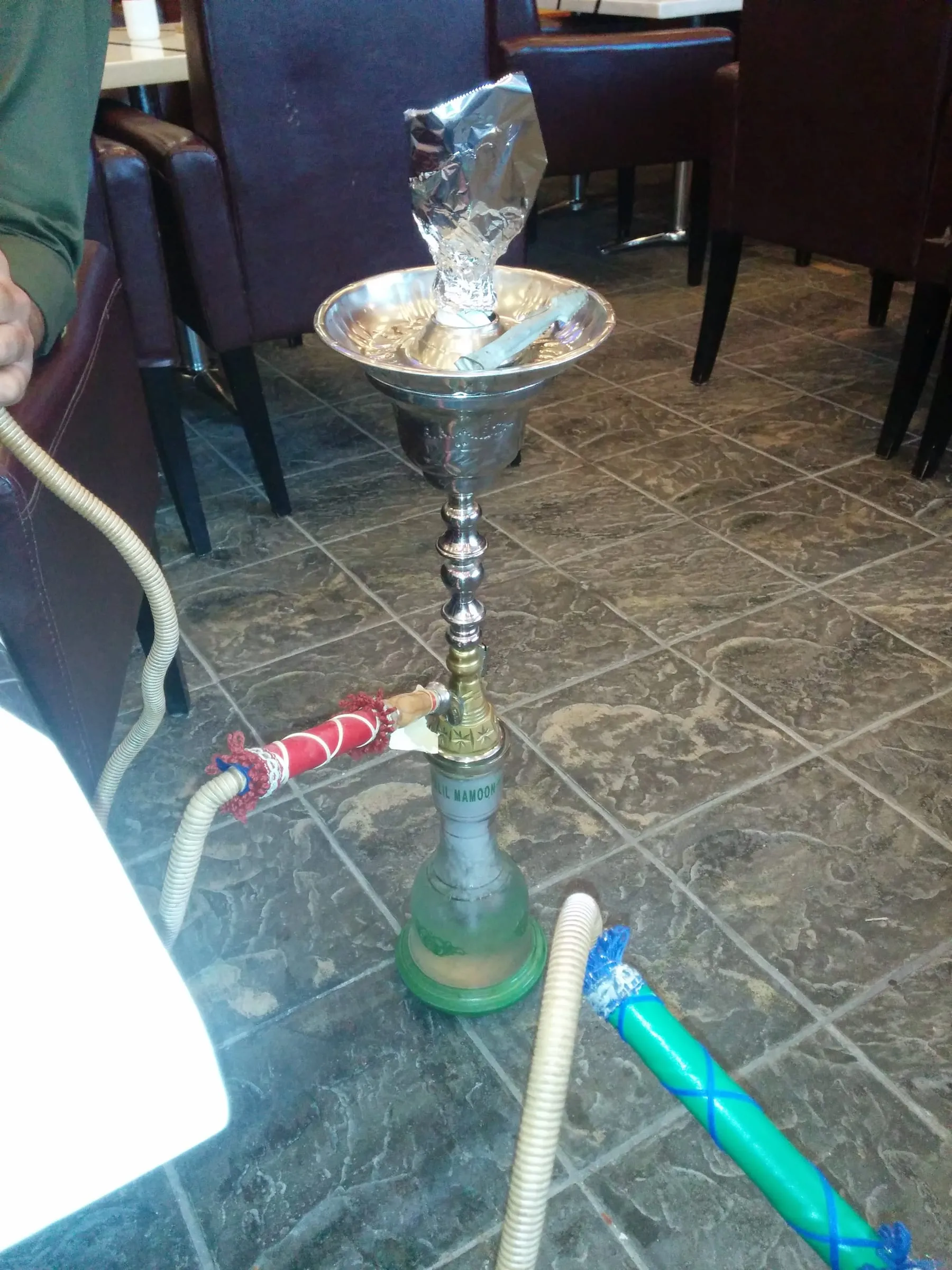 A shisha pipe standing on a tiled café floor beside a table