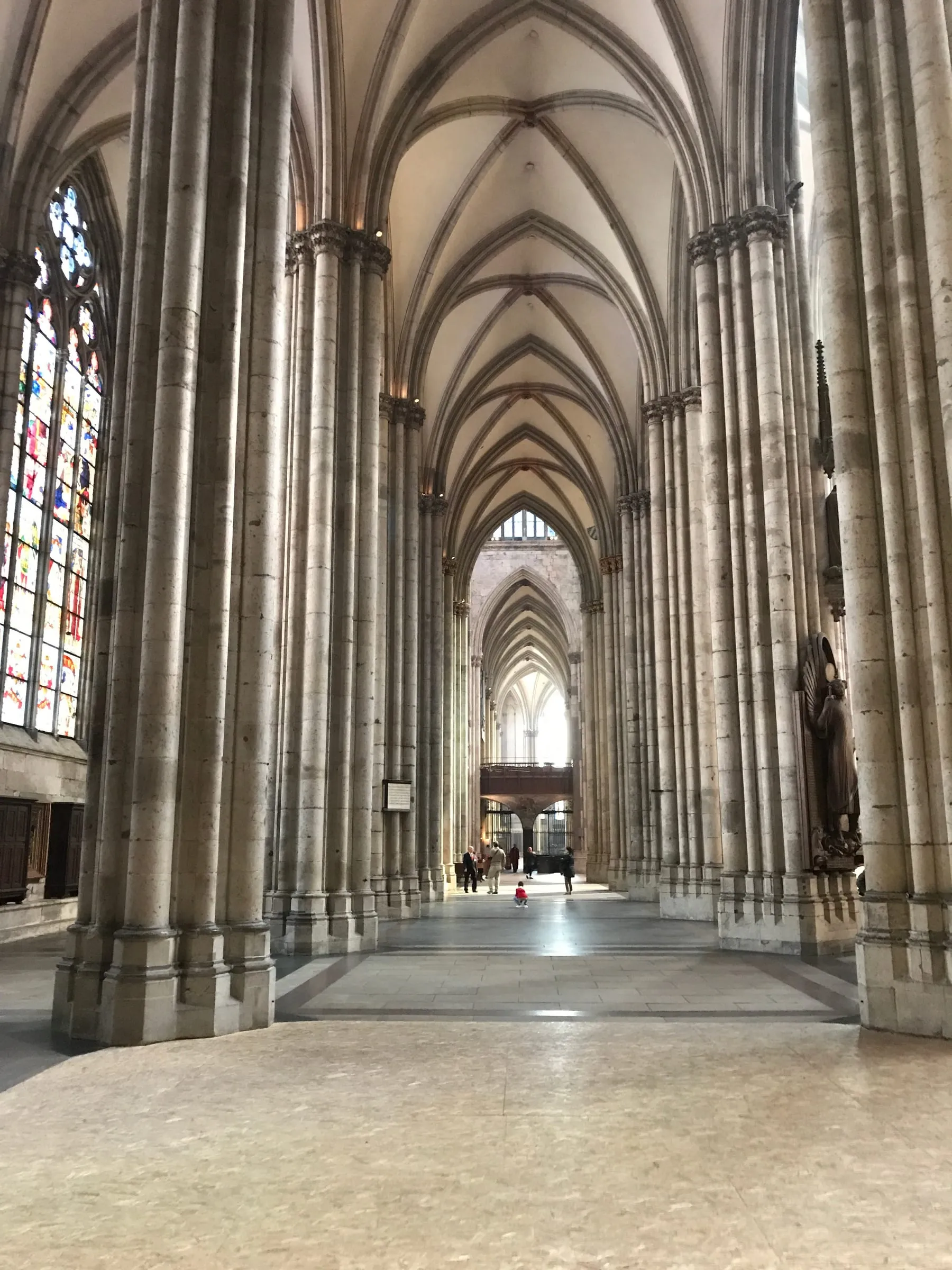 A long side aisle of the cathedral, stone columns and a vaulted ceiling receding into the distance