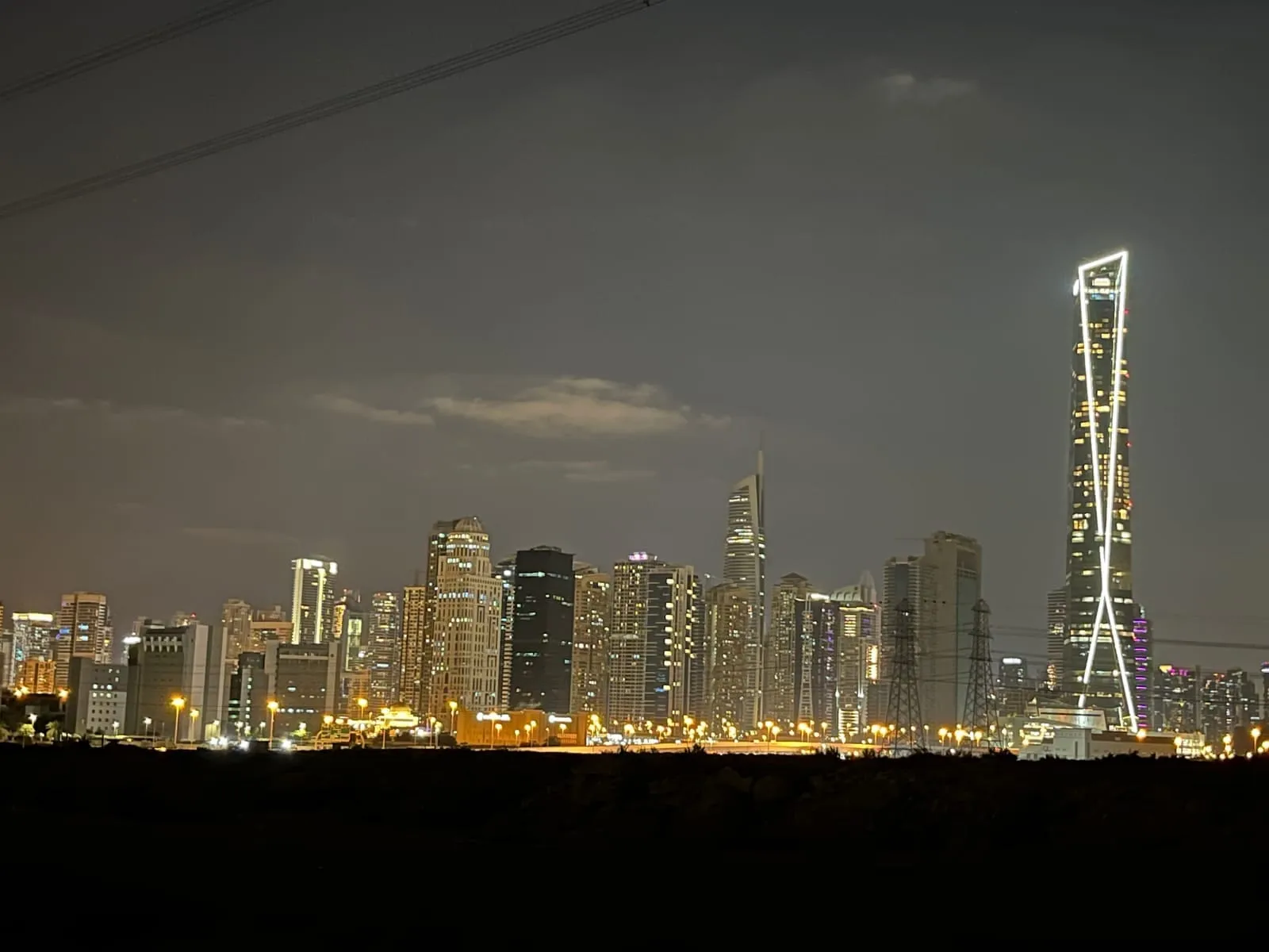 A night skyline seen from open ground, one tall tower outlined in white light