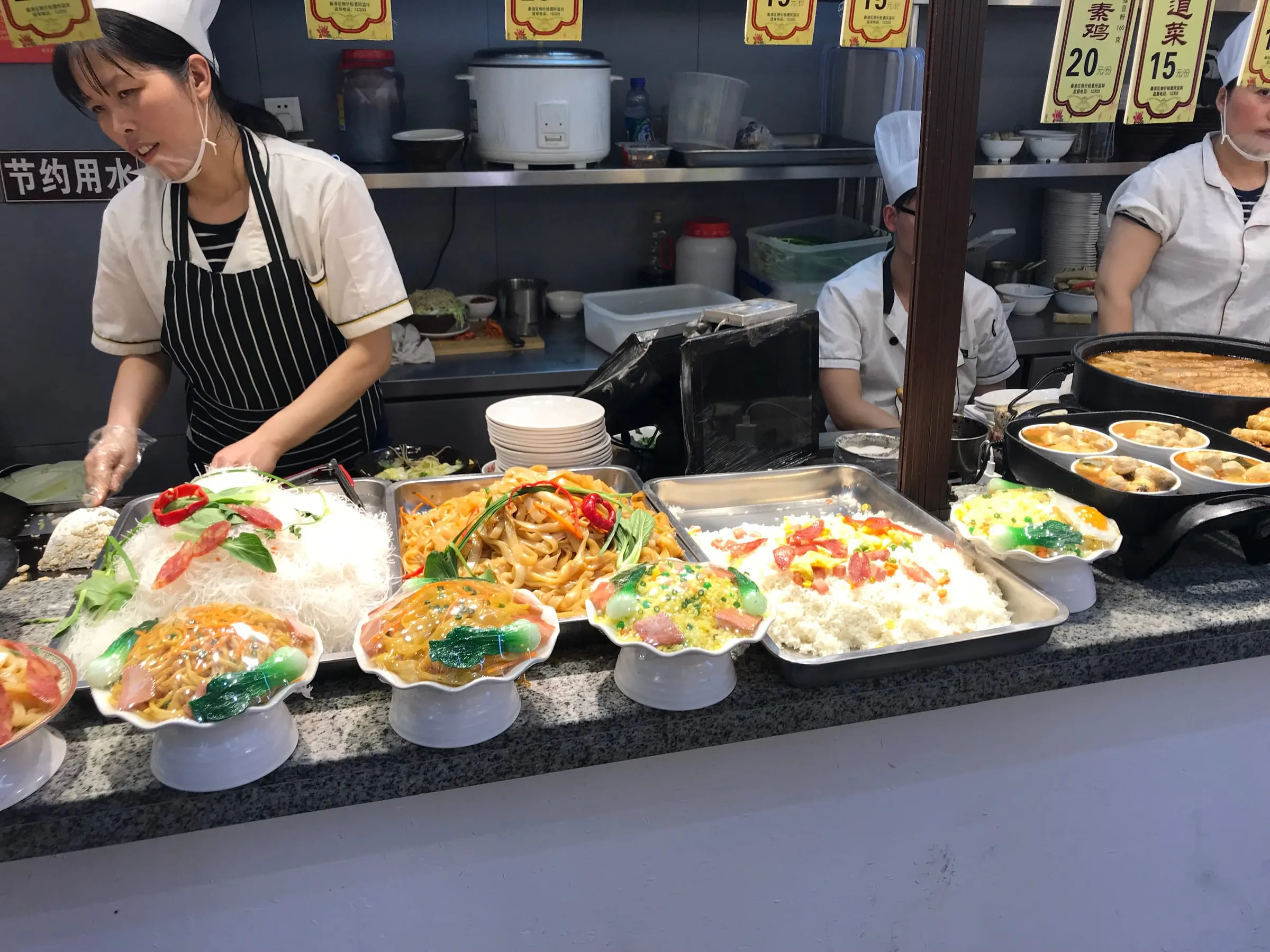 Cooks in white hats at a street food counter, trays of colourful dishes in front