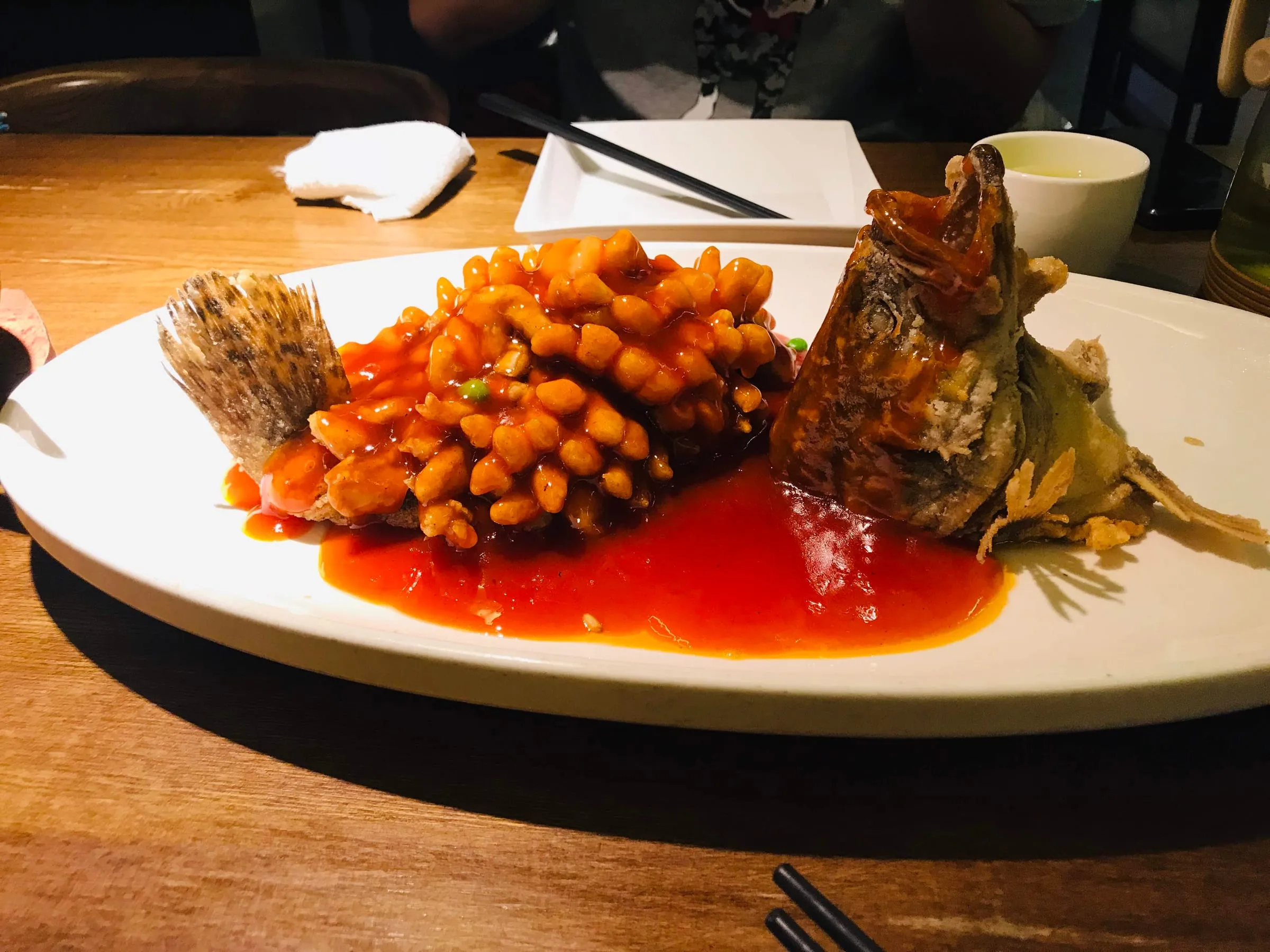 A whole fish cut and fried into crisp curls, in a bright sweet and sour sauce on a white plate