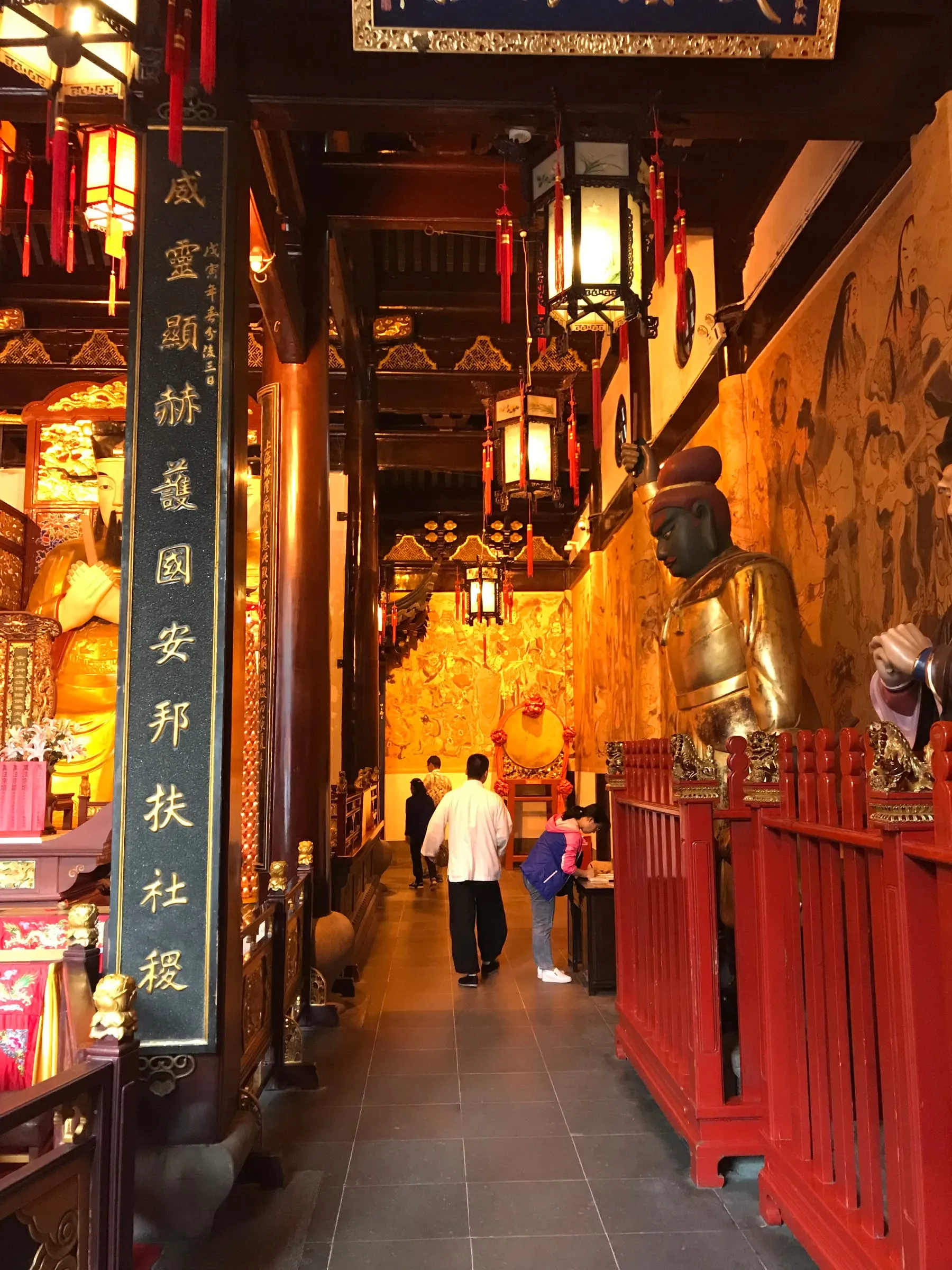 A narrow temple corridor of red pillars, lanterns and carved gold panels