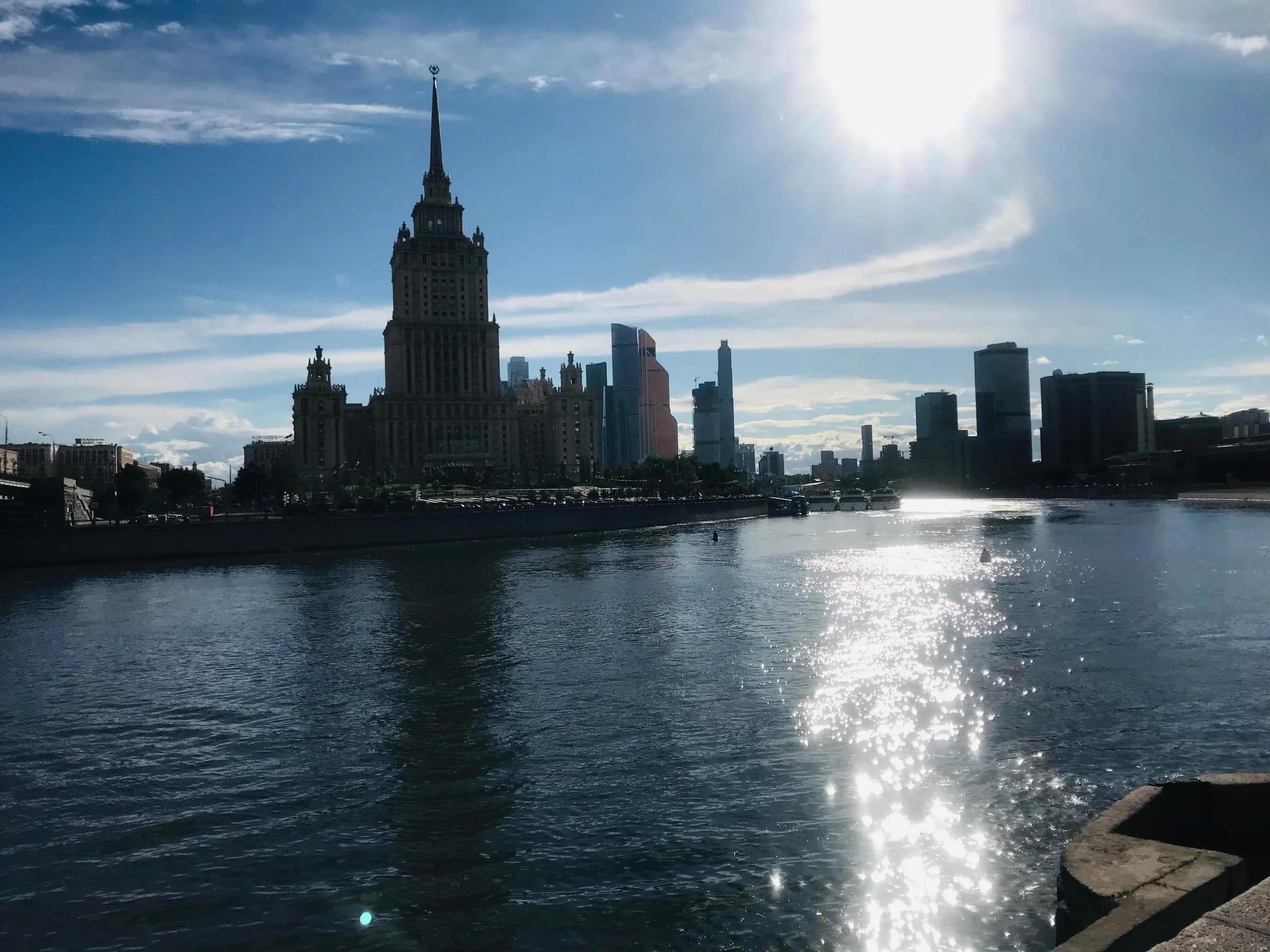 A tall Stalin-era tower in silhouette across the river, sunlight glittering on the water