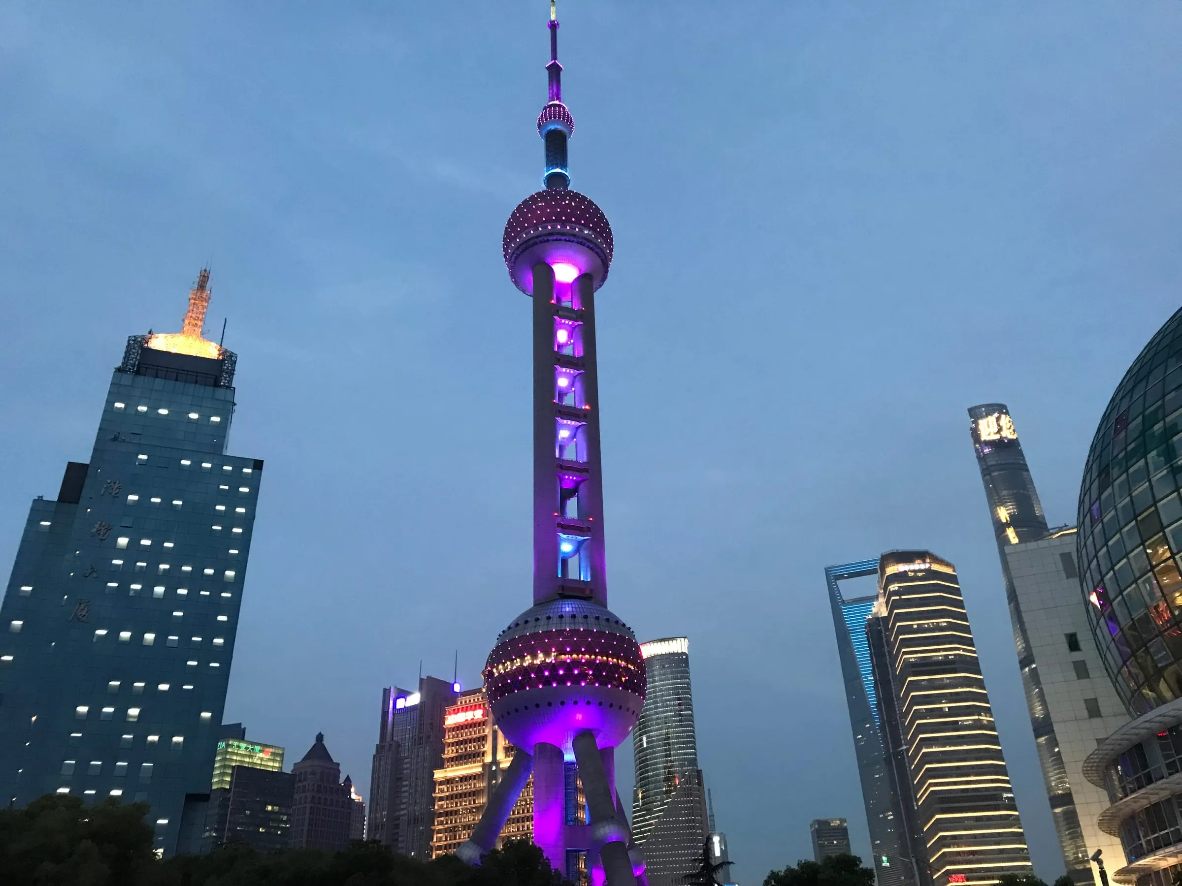 The Oriental Pearl Tower lit purple at dusk, glass towers around it