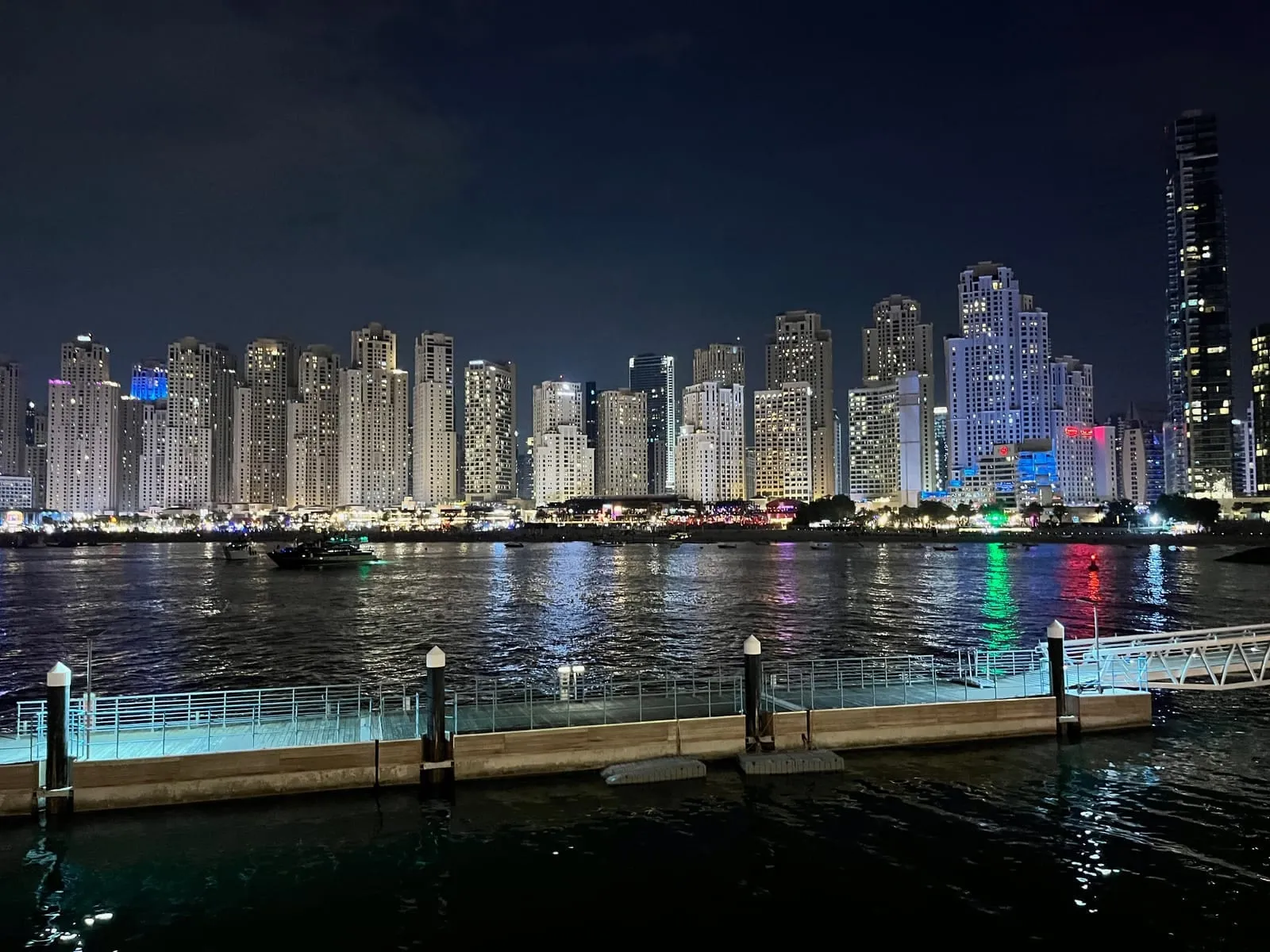 A long row of lit residential towers seen across dark water from a jetty at night