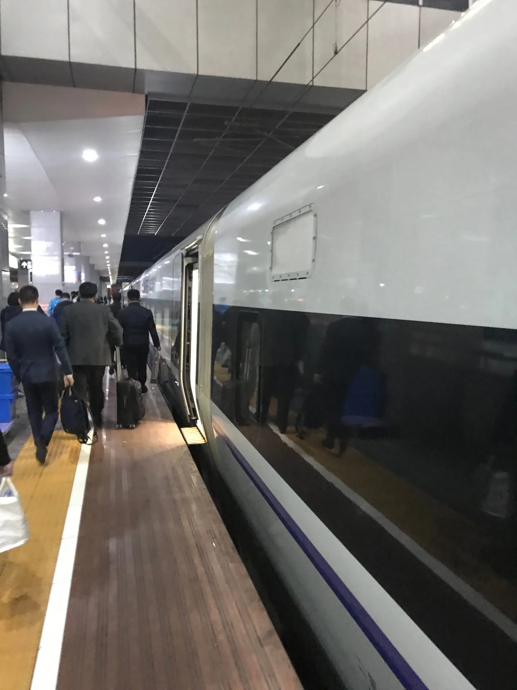 A long station platform at night beside a white high-speed train, passengers walking with bags